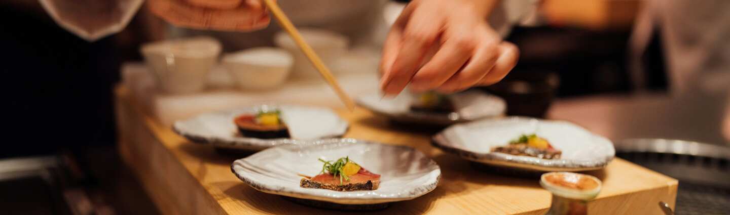 Chef finalizando pequenos pratos de comida japonesa.