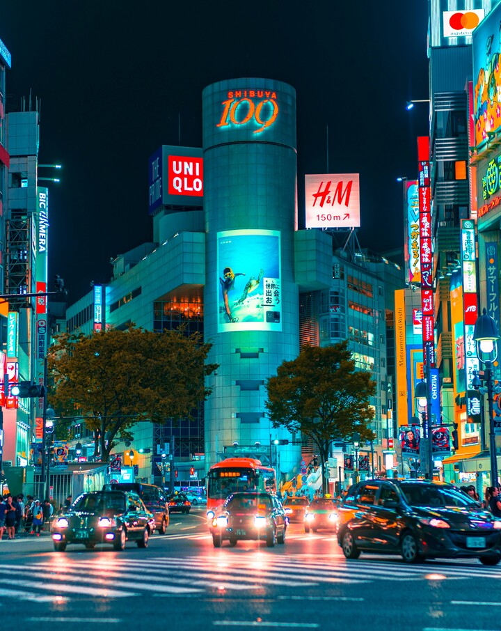 Cruzamento iluminado por letreiros de neon à noite.